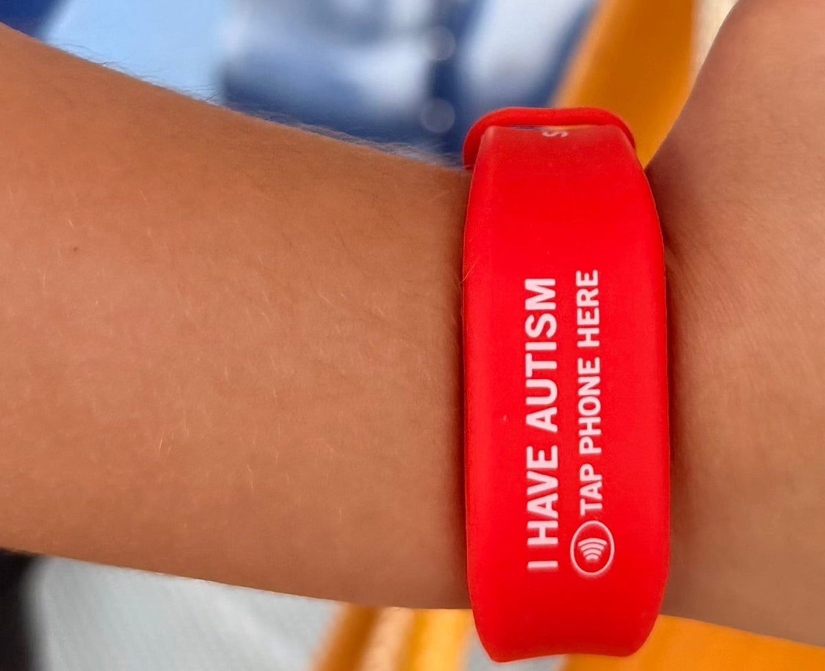 Red wristband with 'I have Autism' text on a person's wrist, blurred background